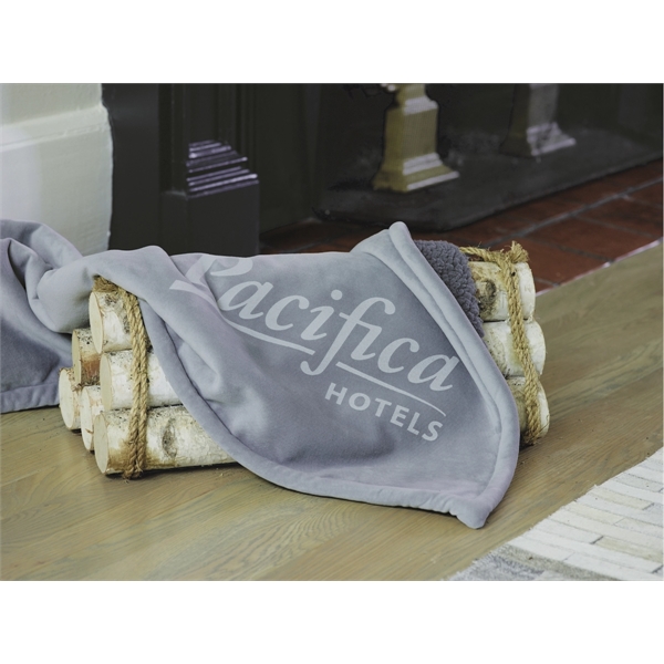 gray with with white branding Newcastle Sherpa Blanket covering firewood